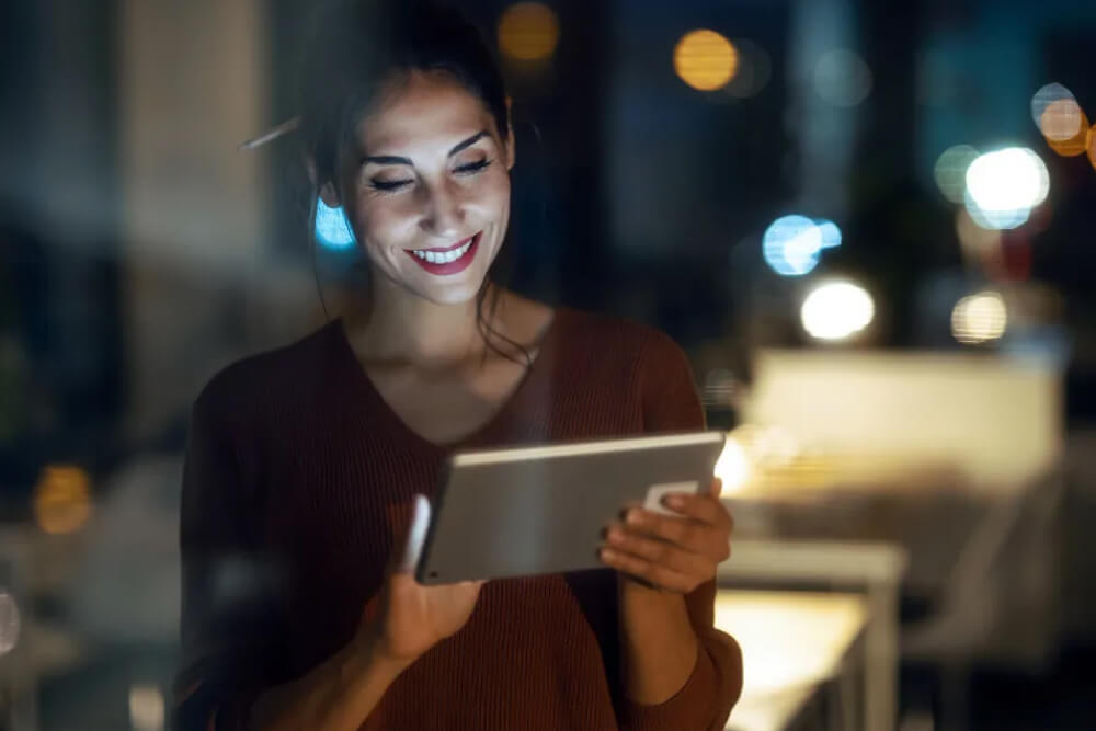 A woman happily using a tablet computer at night.