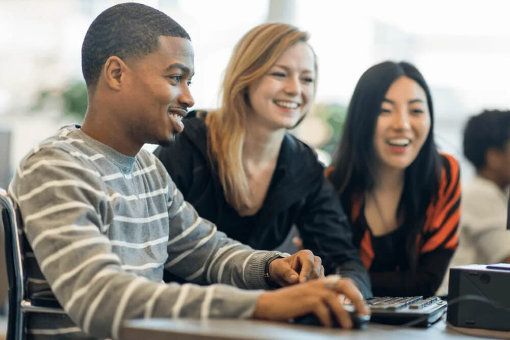 Three college students sit around a computer.