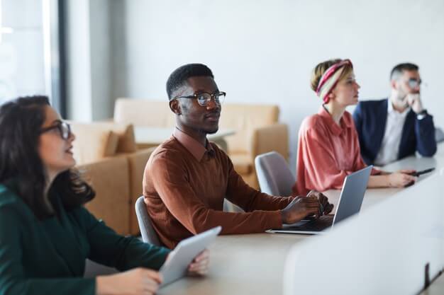 A diverse group of individuals sitting around a table, engrossed in their work on laptops.