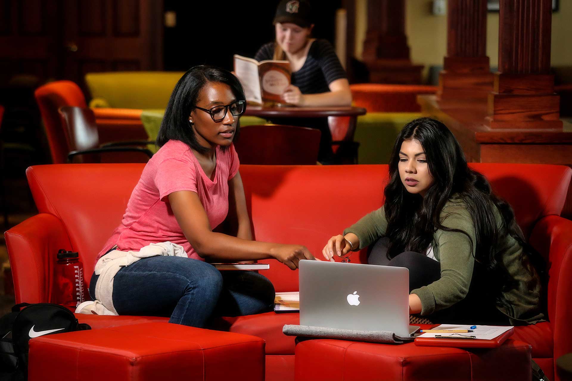 Two students studying on laptops in library.