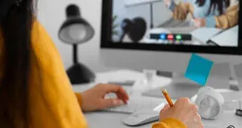 A woman sitting at a desk, using a computer screen and holding a pen to work.