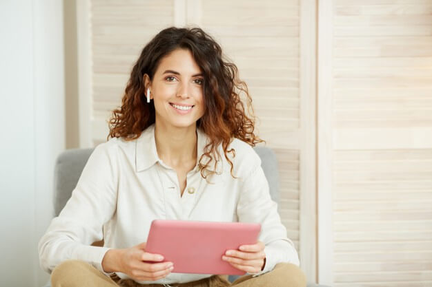 A woman sitting on a couch, engrossed in using a tablet computer.