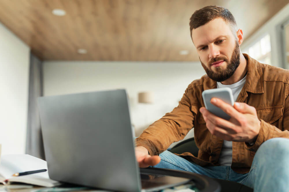 A serious freelancer man using phone and laptop.