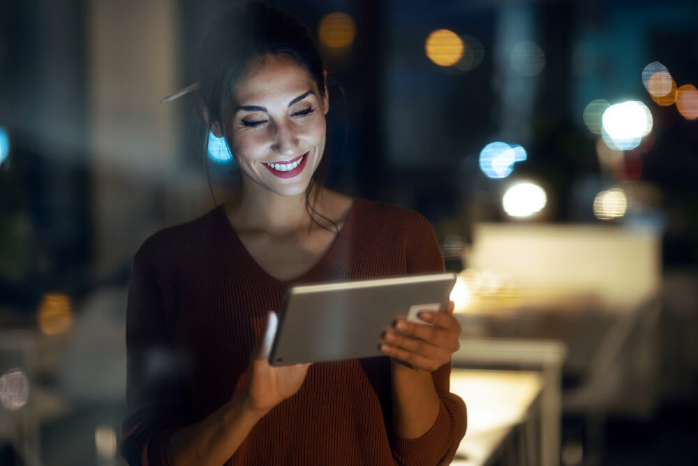 A woman happily using a tablet computer at night.