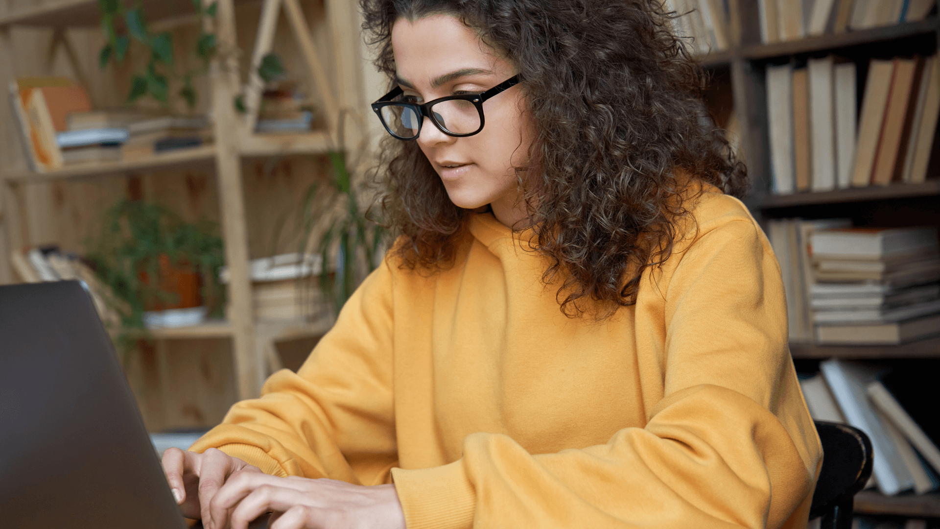 A girl sitting in front of a laptop, focused on the screen, typing and working diligently.